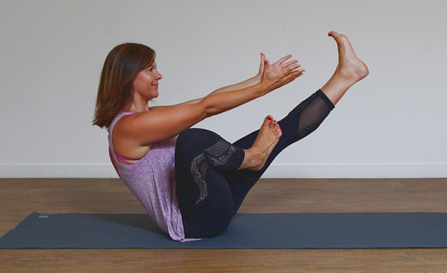 Een vrouw doet een variant op de boat pose bij een core flow yogales.